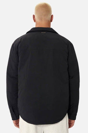 A person with short, bleached blond hair is seen from behind wearing the Industrie The Twin Cullman Jacket in black and light-colored pants, standing against a plain light gray background, embodying the signature Industrie style.