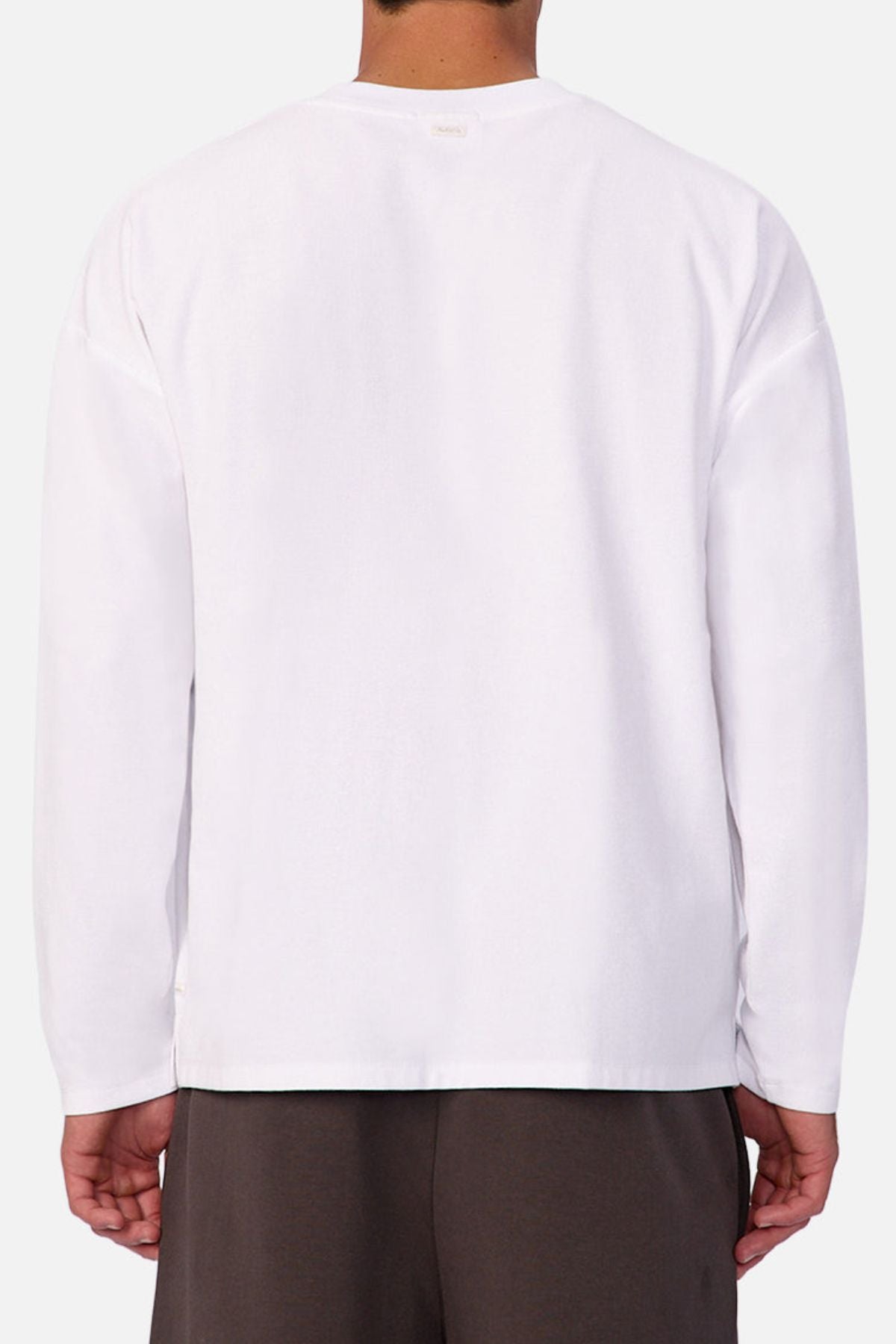 A person is shown from the back against a light background, wearing the Industrie The Waffle Long Sleeve Tee in plain white with dark pants. The tee’s subtle waffle knit texture adds a stylish touch.