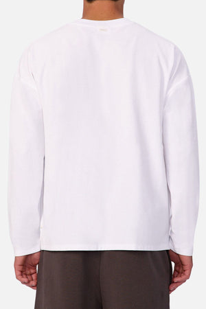 A person is shown from the back against a light background, wearing the Industrie The Waffle Long Sleeve Tee in plain white with dark pants. The tee’s subtle waffle knit texture adds a stylish touch.