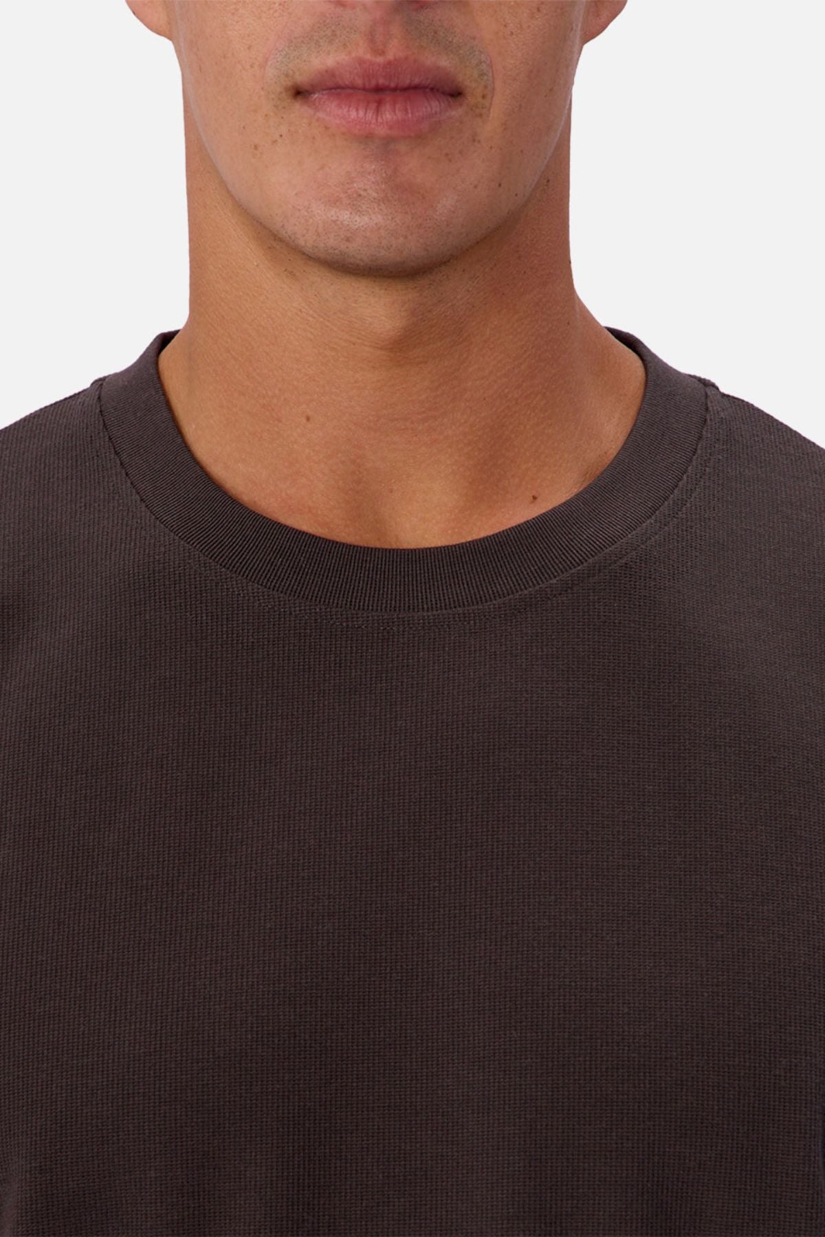 A close-up shows a person wearing the Industrie The Waffle Long Sleeve Tee in dark brown, featuring a textured waffle knit, with only their lower face, neck, and upper chest visible.