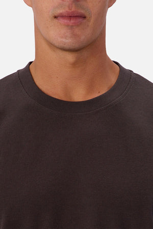 A close-up shows a person wearing the Industrie The Waffle Long Sleeve Tee in dark brown, featuring a textured waffle knit, with only their lower face, neck, and upper chest visible.