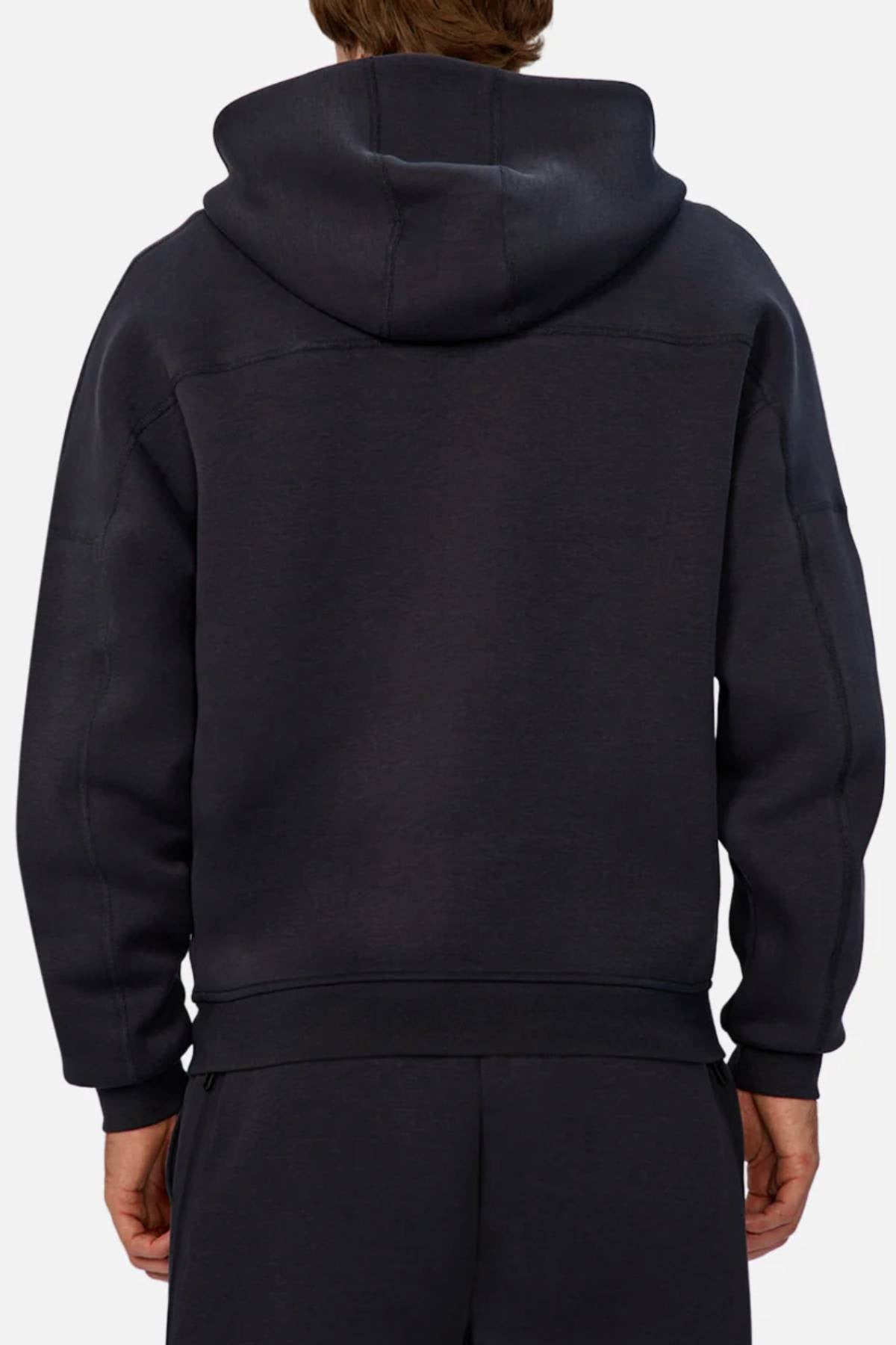 A person is seen from behind wearing the Industrie The Washington Zip Thru jacket and matching black pants. The loose-fit jacket, ideal for everyday wear, has the hood up but not covering their head.