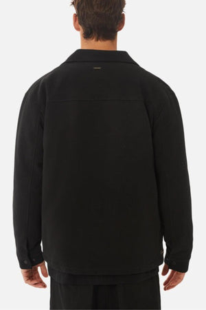 A man faces away from the camera, wearing the Industrie The Westport Jacket in black with long sleeves, a collar, and twin chest pockets, set against a plain light background.