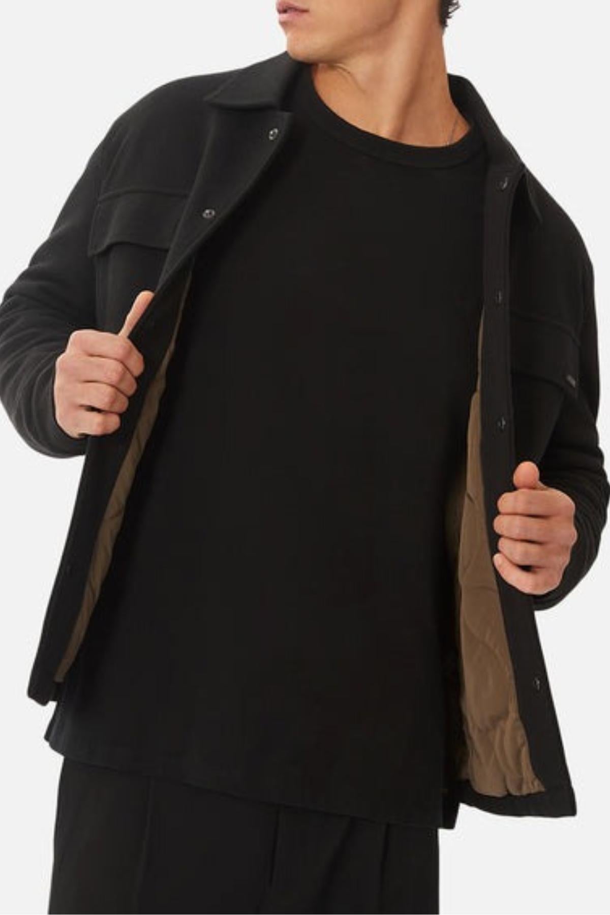 A person wearing a black shirt and the Industrie The Westport Jacket with a light brown quilted lining, holding the jacket open with both hands. The image is cropped at the neck and waist.