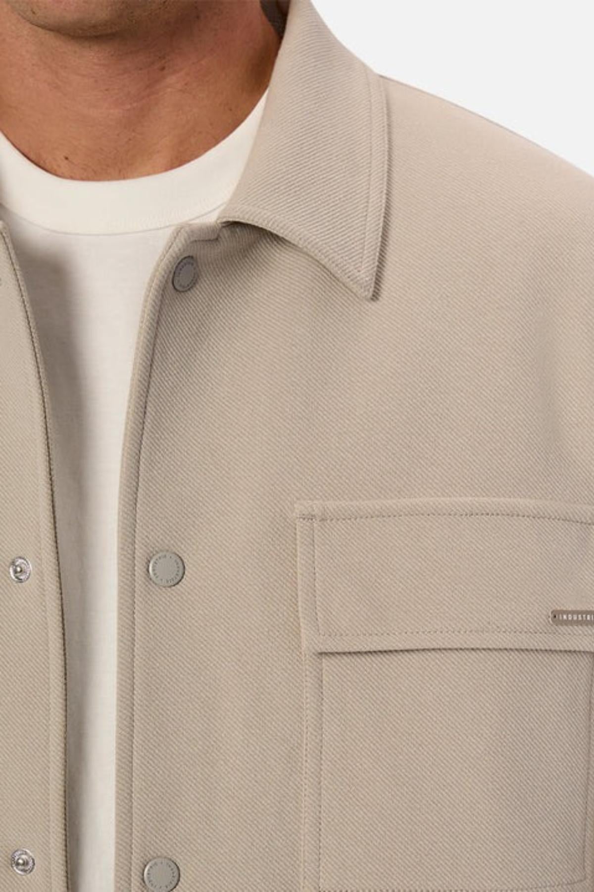 Close-up of a person wearing the Industrie The Westport Jacket in light beige with snap buttons over a white T-shirt, highlighting part of the chest, collar, and one textured twin chest pocket.