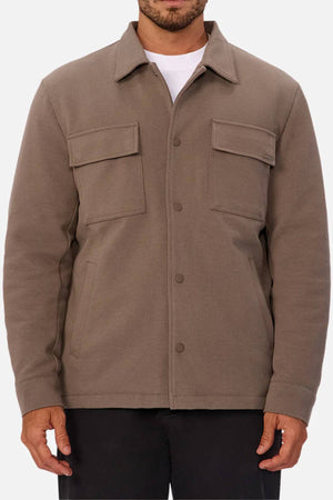 Someone wearing the Industrie The Westport Jacketโa taupe menโs jacket featuring chest flap pockets, side pockets, and a classic collarโover a white shirt and black pants; an ideal choice for everyday style.