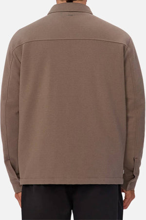A person is seen from the back against a plain light background, wearing the Industrie The Westport Jacket in taupe. The jacket has long sleeves, a straight hem, twin chest pockets, and press stud buttons.