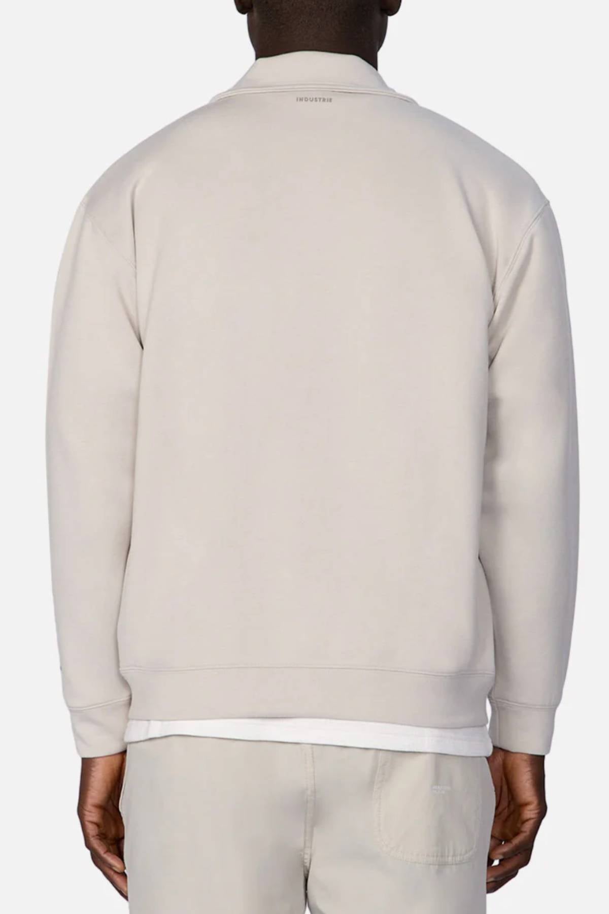 A person in the Industrie The Zip Thru Track Top and matching pants is shown from behind, with short hair above the collar. Subtle INDUSTRIE branding stands out against a plain, light background.
