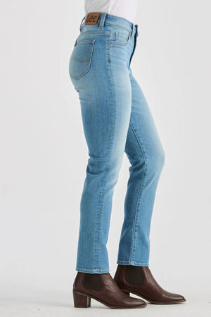 Person wearing Lee Originals LMW Mid Rise Slim Jean in light blue denim and dark brown block-heeled ankle boots, shown from the side and waist down against a plain light background.