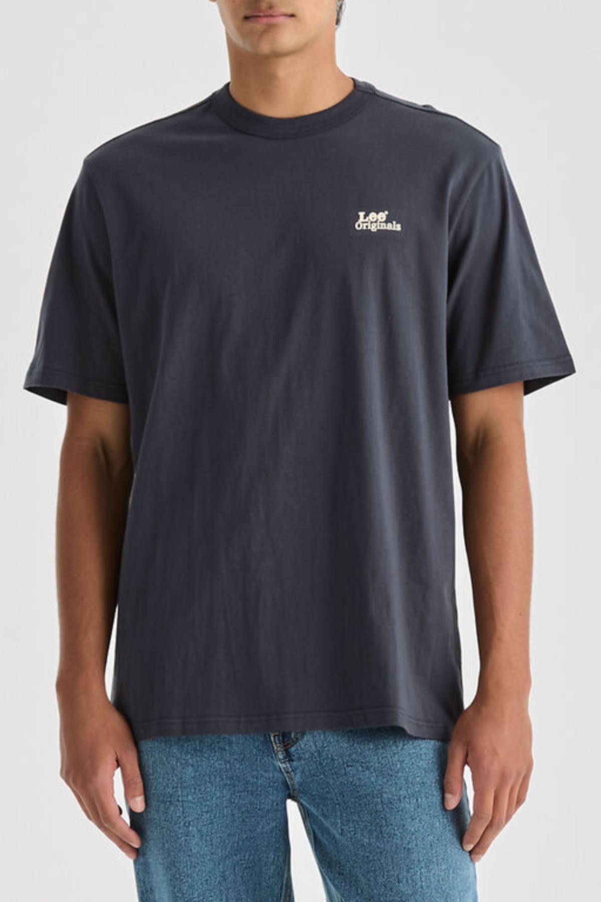 A person wears a relaxed-fit, 100% cotton dark gray Lee Originals Relaxed Tee with "Originals" in white on the left chest, paired with light blue jeans, standing against a plain background.