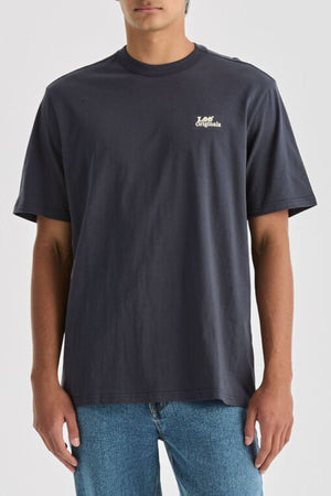 A person wears a relaxed-fit, 100% cotton dark gray Lee Originals Relaxed Tee with "Originals" in white on the left chest, paired with light blue jeans, standing against a plain background.