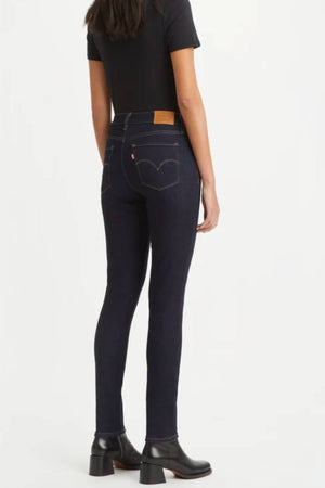 Someone in Levi's 311 Shaping Skinny Jean (dark blue), a black short-sleeve top, and black heeled ankle boots stands with their back to the camera against a plain light background.