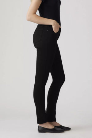 A person models the Levis 311 Shaping Skinny Jean in black, paired with a fitted black t-shirt and black flats. They stand against a plain light gray background in a side profile, shown from shoulders down with one hand in their pocket.