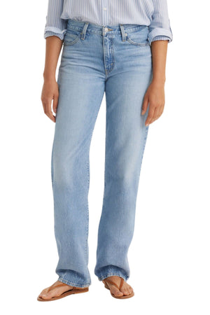 A person in Levi's '94 Baggy Jean (light blue, mid-rise), a matching light blue striped shirt tucked in, and tan flip-flops stands against a plain white background.