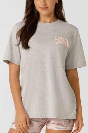 A woman wearing a breathable cotton Lorna Jane Heartbeat Relaxed T-Shirt in light gray and pink palm tree shorts, standing against a plain background.