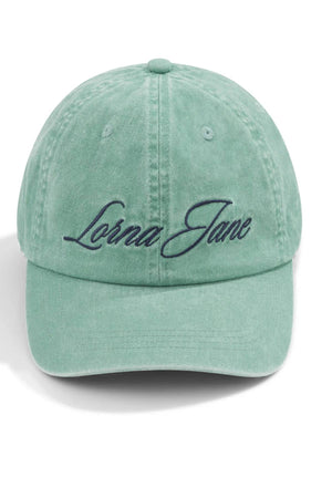The Lorna Jane Heritage Washed Logo Cap in light green features "Lorna Jane" embroidered in dark script on the front. This vintage-style cap is shown against a plain white background.