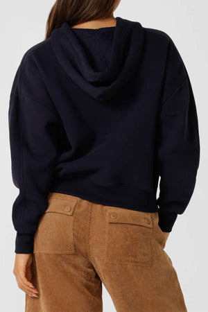 A person is shown from the back wearing a black Lorna Jane Limited Edition Lotus Hoodie and light brown corduroy pants, with their right hand resting by their side.