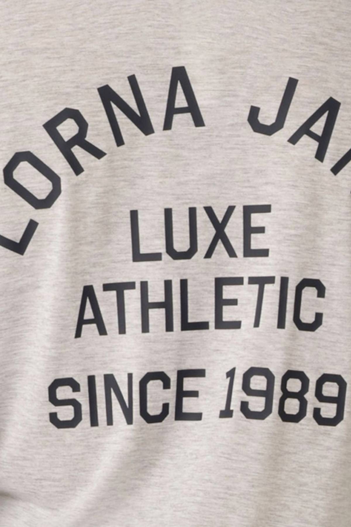 Close-up of light gray fabric from the Lorna Jane Limited Edition Lotus Long Sleeve Top, featuring bold black text: "LORNA JANE LUXE ATHLETIC SINCE 1989," adding a stylish detail to this exclusive piece.