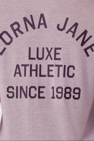 A close-up of the Lorna Jane Limited Edition Lotus Long Sleeve Top in mauve, featuring bold black text: "LORNA JANE LUXE ATHLETIC SINCE 1989." This exclusive long sleeve piece elevates your activewear collection.