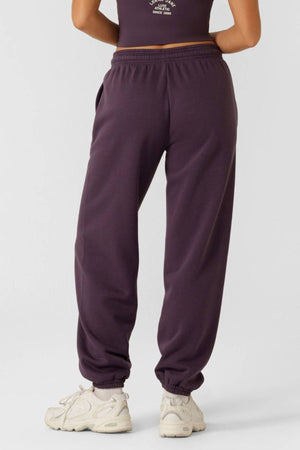 A person in high-waisted, loose-fitting Lorna Jane Limited Edition Lotus Sweatpants and white sneakers stands with their back to the camera against a plain background.