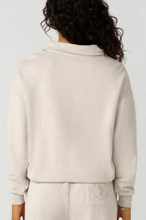 A person with long, curly dark hair is seen from behind wearing a light beige Lorna Jane LJC Heritage Quarter Zip Sweat and matching sweatpants, made from plush cotton terry for a soft, comfortable look with minimal visible details.