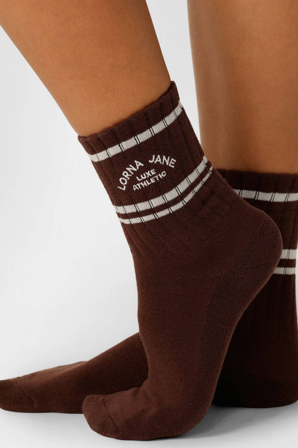 Close-up of a person wearing Lorna Jane Lotus Crew Socks in brown with white stripes and "Lorna Jane Luxe Athletic" embroidered around the ankle.