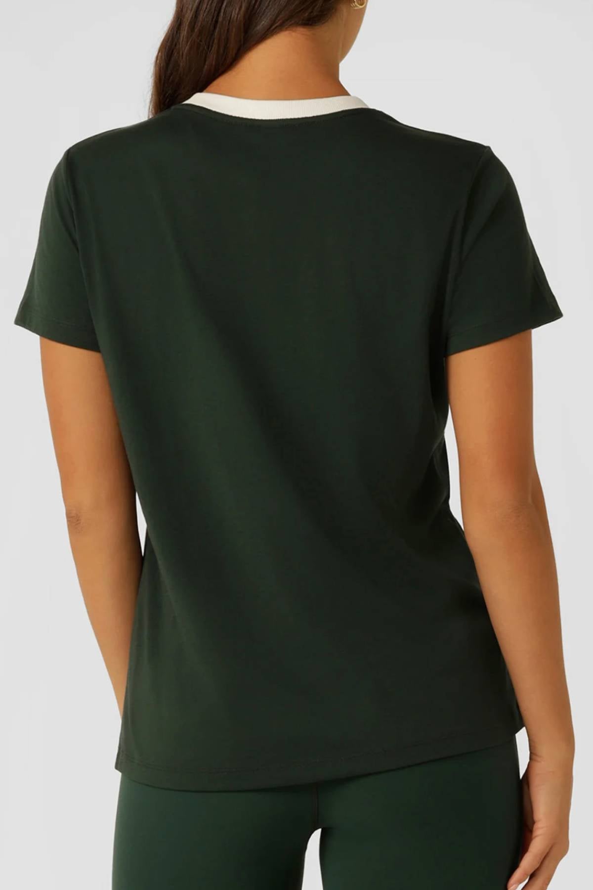 A person with long brown hair is seen from the back, wearing the Lorna Jane Lotus Heritage Ringer T-Shirt in dark green with a white collar and matching pants against a plain, light background.