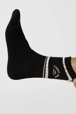 Someone wears the Lorna Jane Lotus Limited Edition Quarter Crew Socks—black quarter crew style with two white ankle stripes and “Lorna Jane Active” text—foot extended against a plain white background.