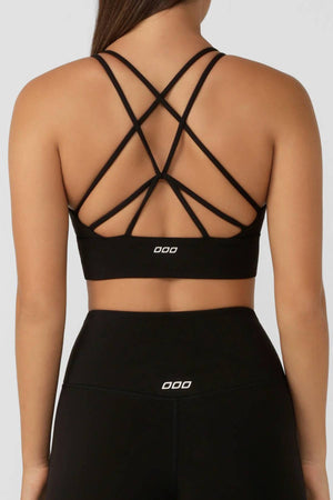 A woman wears the Lorna Jane Lotus Longline Sports Bra in black, featuring moisture-wicking fabric and multiple crisscross back straps, paired with matching high-waisted leggings. Both have a small white logo and are shown from the back for style and comfort.