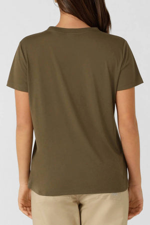 A person with long brown hair, seen from behind, wears an olive green Lorna Jane Lotus T-Shirt and light beige pants against a plain light gray background.