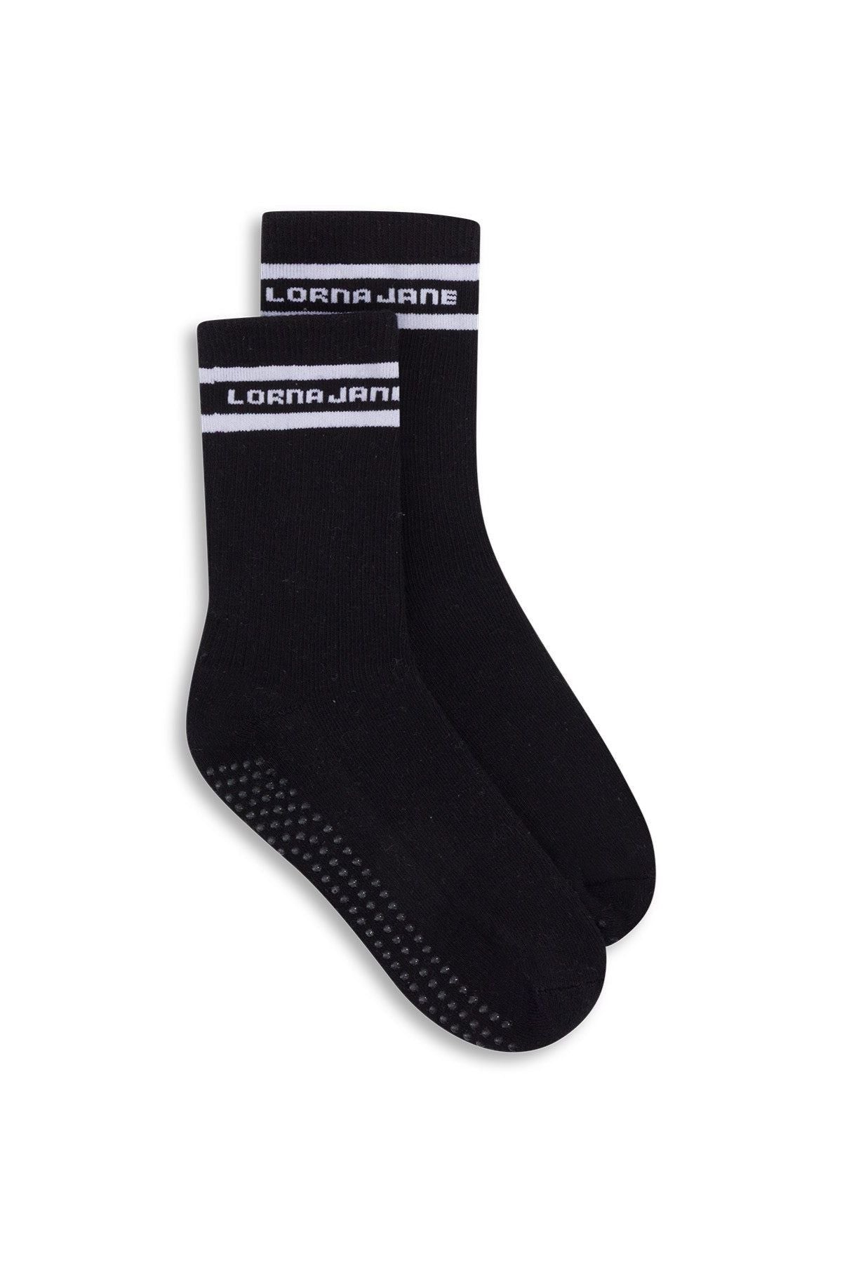 The Lorna Jane Pilates Grip Crew Socks are black crew socks featuring a white stripe and "LORNA JANE" text at the top. Designed specifically for Pilates, these socks have a grippy sole with small non-slip dots on the bottom to provide enhanced stability and support.