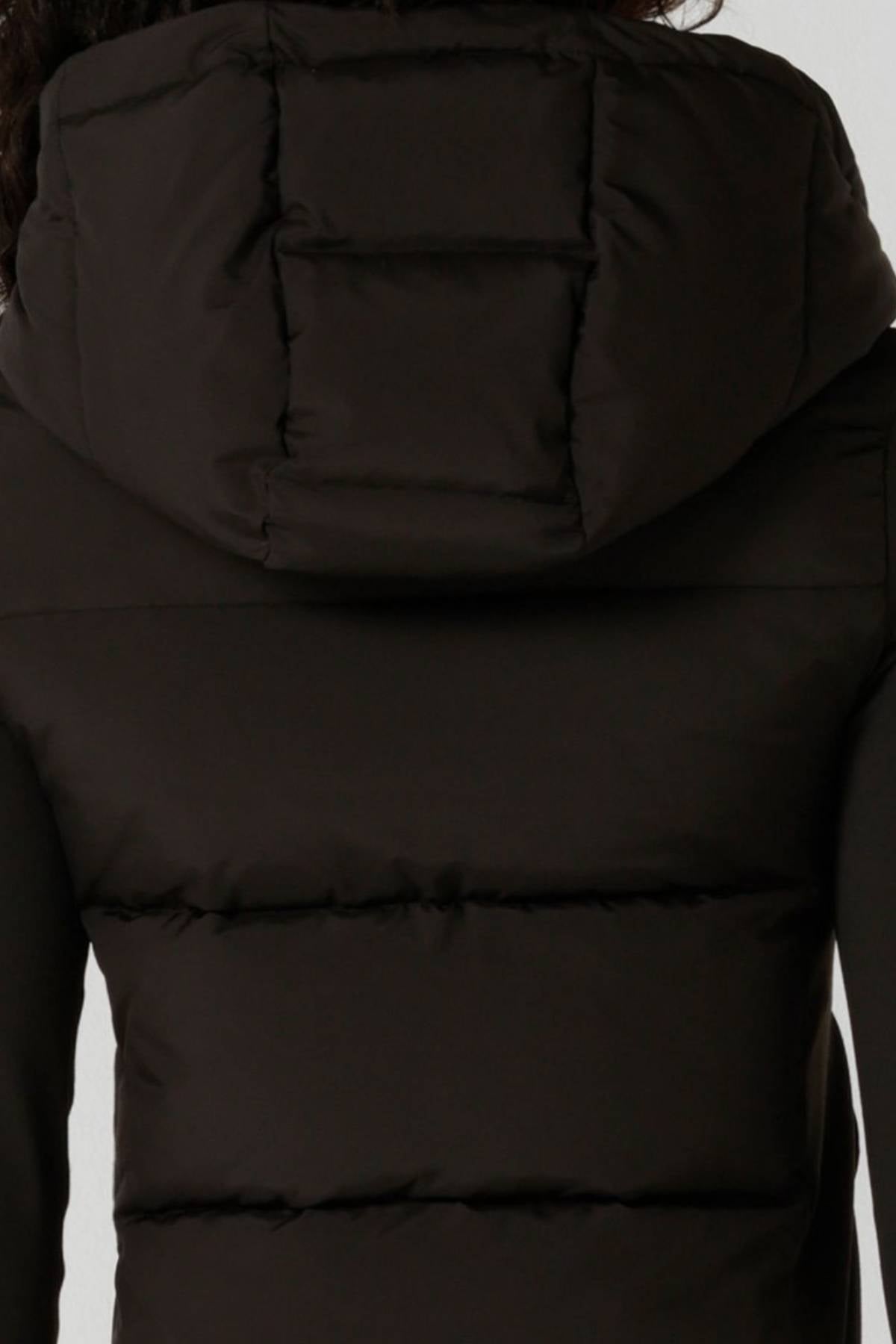 A close-up of the back of a person wearing the Lorna Jane Warm Up Thermal Combo Puffer in black, featuring an adjustable hood, horizontal stitching, and thick insulated material.