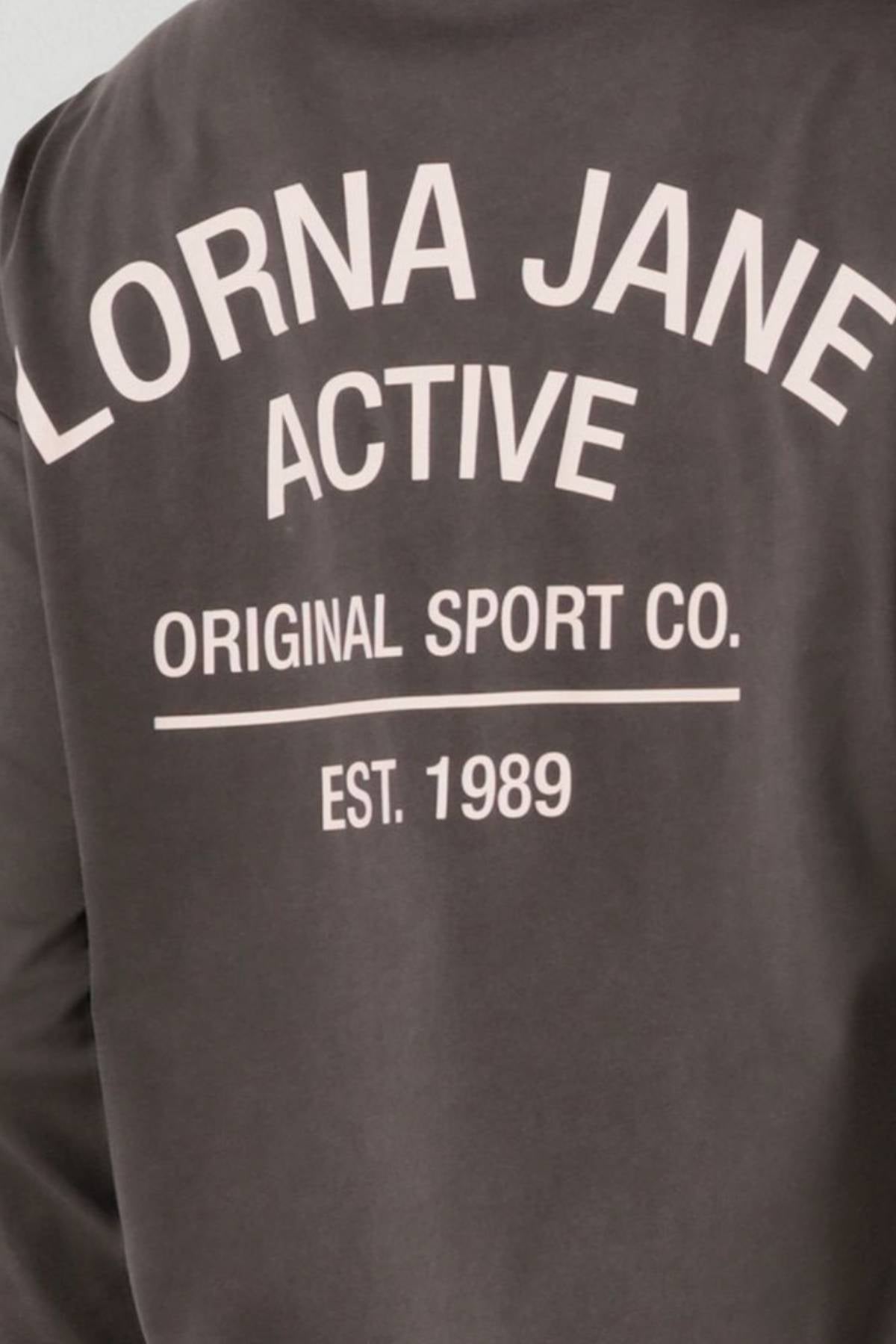 Back view of the Lorna Jane Washed Original Sport Long Sleeve, a dark vintage-wash sweatshirt with white text: "LORNA JANE ACTIVE ORIGINAL SPORT CO. EST. 1989.
