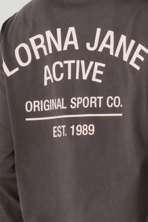 Back view of the Lorna Jane Washed Original Sport Long Sleeve, a dark vintage-wash sweatshirt with white text: "LORNA JANE ACTIVE ORIGINAL SPORT CO. EST. 1989.