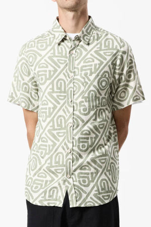 A person wearing the Mr Simple Earl Short Sleeve Shirt with a loose fit and geometric green and white pattern pairs it with black pants, standing forward with hands behind their back.