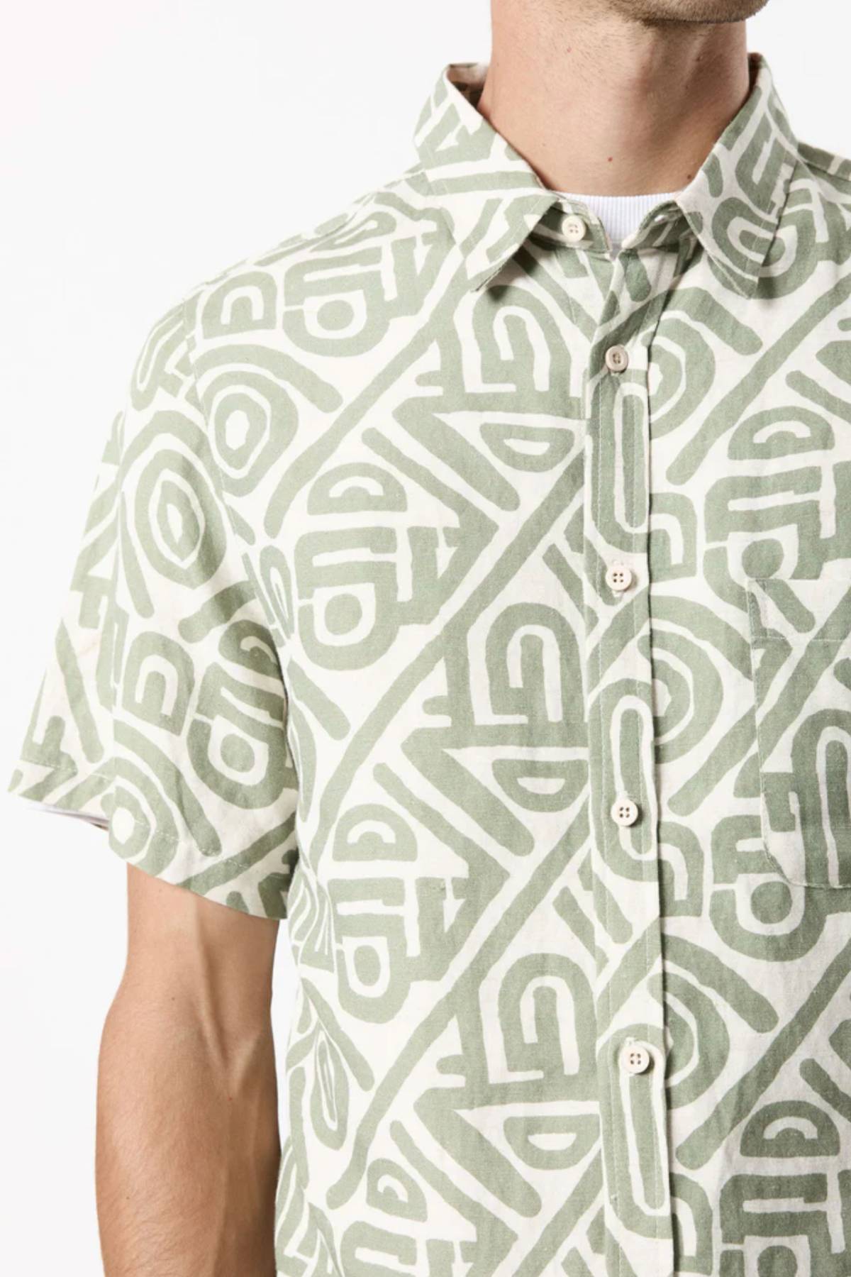 A person is wearing a Mr Simple Earl Short Sleeve Shirt in light green and white with a geometric pattern, featuring a collar and front buttons, in a loose fit design. The background is plain white.