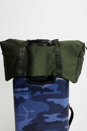 The Mr Simple Nelson Duffle, a quality item, is securely strapped onto the handle of a blue camouflage-patterned suitcase against a white backdrop.