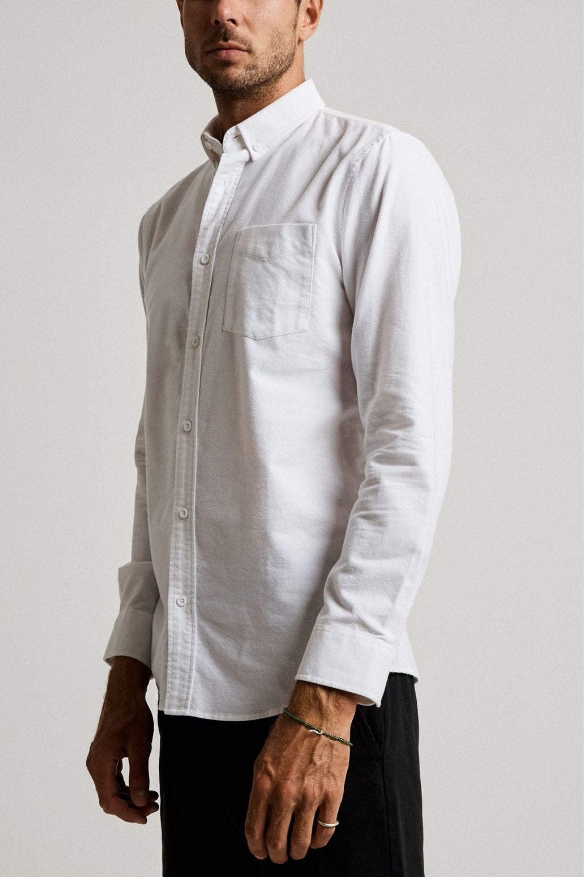 A man wearing the Mr Simple Oxford Shirt—slim-fit, white, 100% cotton with a chest pocket—and black pants stands against a plain light backdrop, facing slightly to the side.
