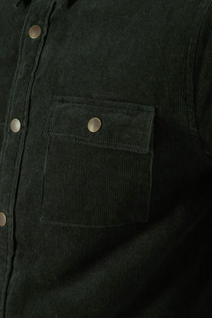 Close-up of the Mr Simple Quilted Cord Jacket in dark green cotton corduroy, highlighting a chest pocket with flap and metal snap closure, plus part of the front placket with matching snap buttons.
