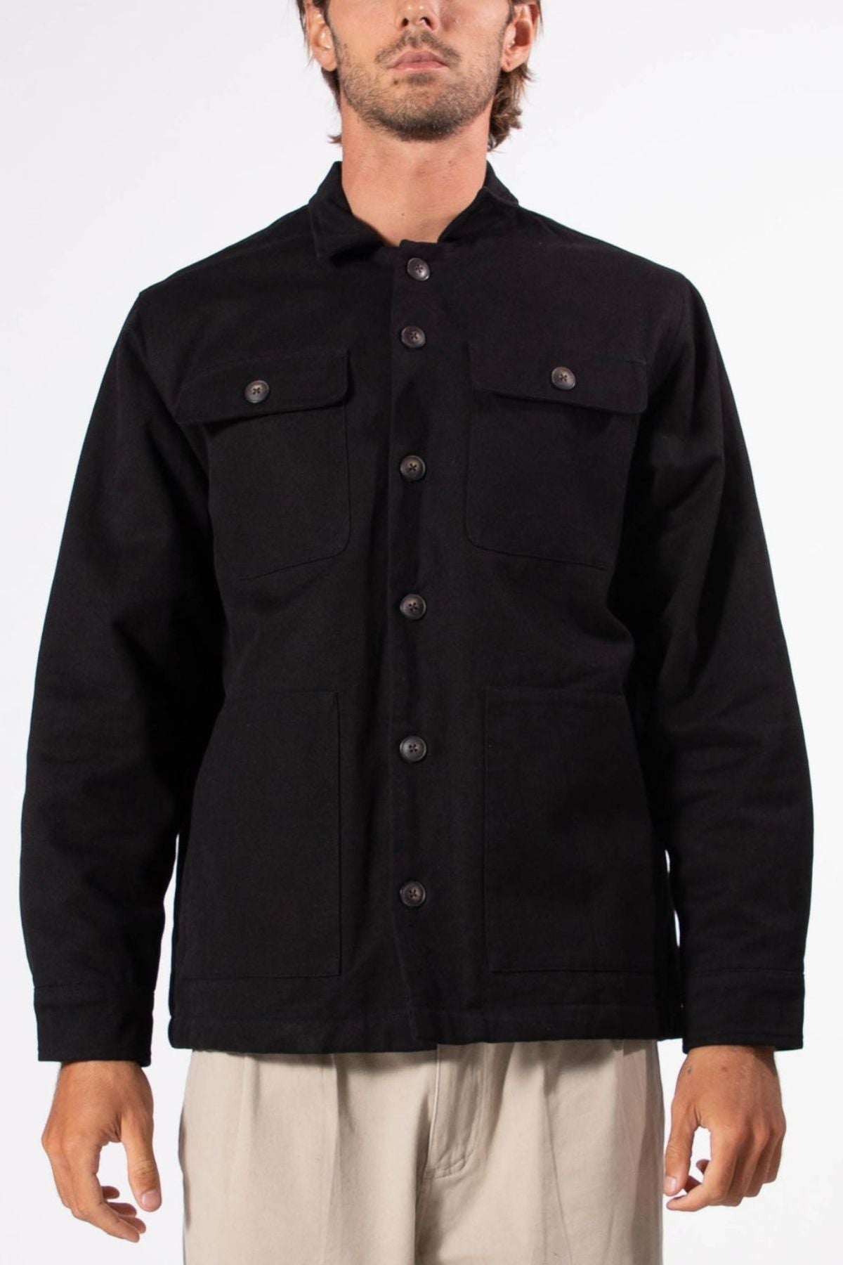 A person wears a Mr Simple Stockyard Sherpa Jacket in black with two chest pockets and beige pants, standing against a plain white background.
