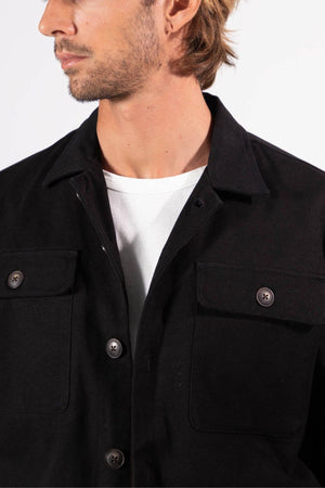A man with light brown hair and facial hair wears the Mr Simple Stockyard Sherpa Jacket in black over a white t-shirt. The cropped photo highlights his head turned sideways and upper torso, showcasing classic Mr Simple style against a plain background.