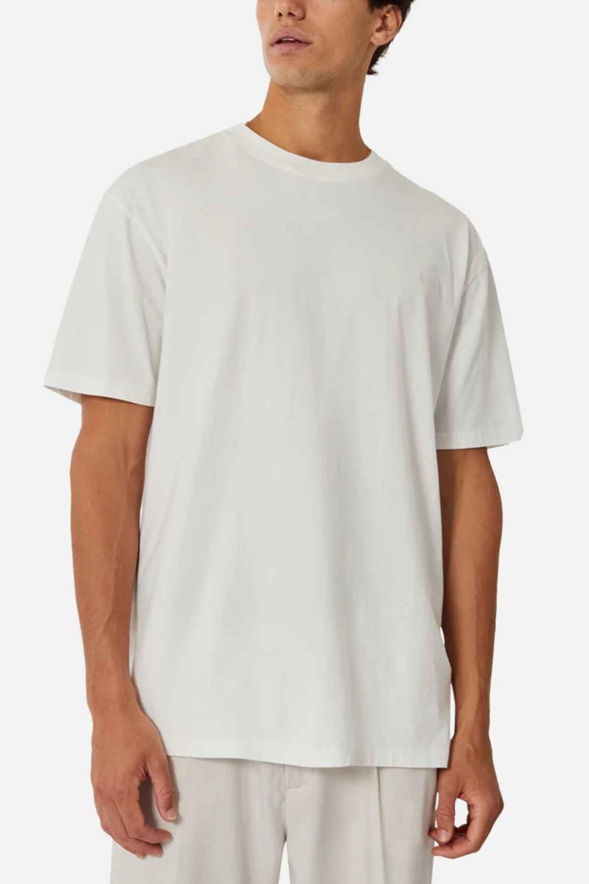 Against a light background, the person wears an oversized Industrie The Del Sur Tee, made from 100% cotton. Their short hair enhances the casual and minimalist look as they gaze slightly to the side.