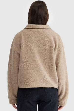 A person with long brown hair, seen from behind, is wearing the ORTC Georgia Sherpa Jacket in beige and black jeans against a plain light background.