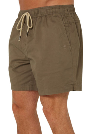 A person wearing Pilbara Cotton Stretch Shorts in olive green, featuring an elastic waist, side pockets, and a small embroidered logo on the left leg. Only the lower torso and upper legs are visible.
