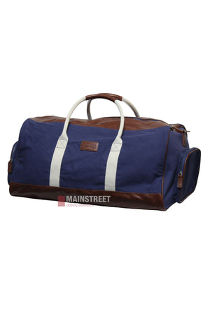 The Pilbara Long Weekender Bag is a blue canvas and leather travel bag with brown leather accents, white handles, and side pockets. It features a rectangular shape and a front patch, shown against a white background.