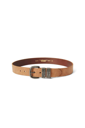 The RM Williams Drover Belt is a light brown leather accessory, crafted from vegetable-tanned leather, and features a weathered silver buckle. It boasts multiple holes for size adjustment and has text stamped on its inner side. The buckle includes an additional silver loop with a decorative engraved design.