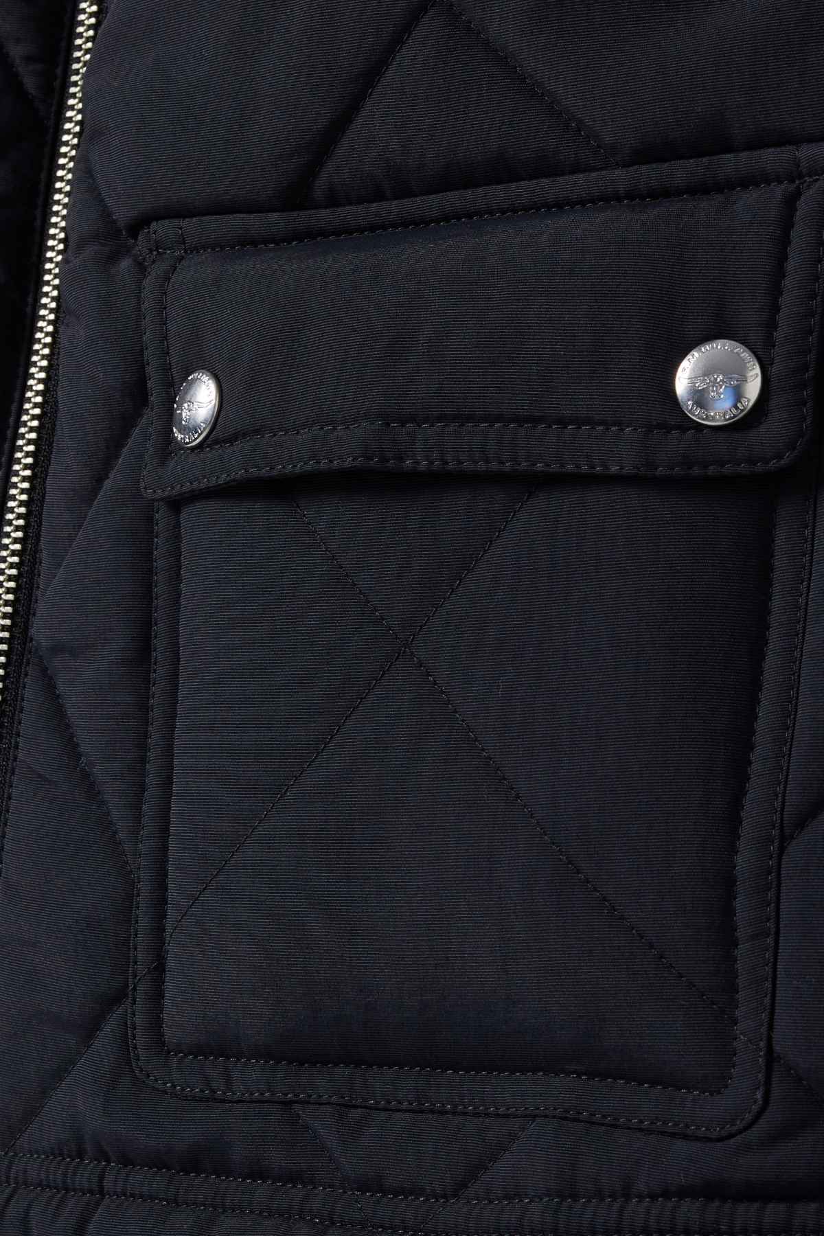 Close-up of a quilted fabric flap pocket with two silver buttons and a visible left-side zipper. The RM Williams Willippa Vest exhibits an X pattern stitch, highlighting its recycled nylon quilting.