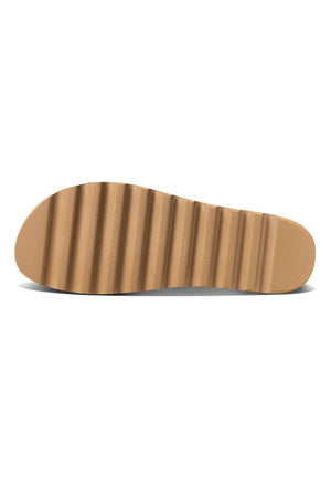 The REEF Cushion Vista Hi features a tan flat sole with a ribbed, wave-like tread pattern. Shown from the bottom, it highlights the unique texture, design details, and built-in arch support for enhanced comfort.