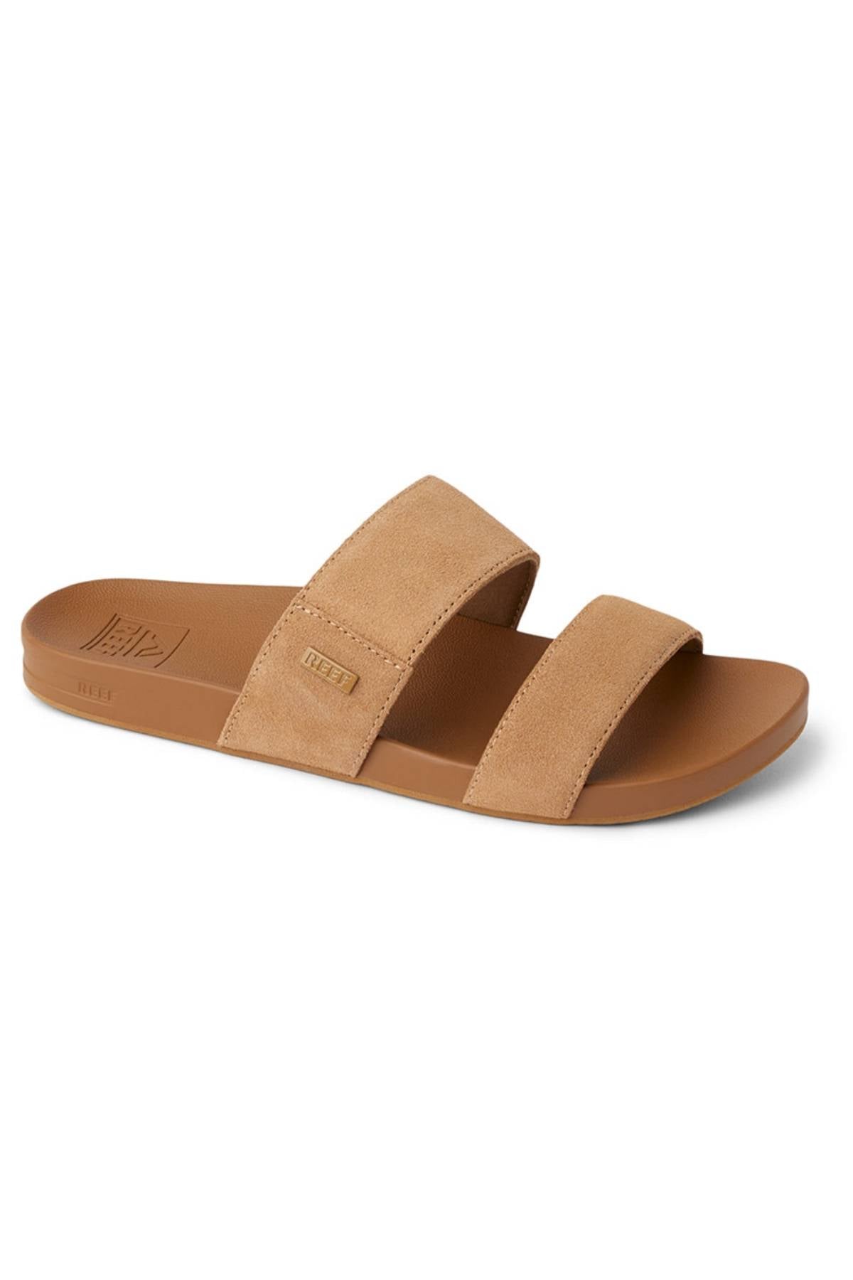 The REEF Cushion Vista Stevie is a tan slide sandal with two wide suede straps and a brown cushioned midsole, combining comfort and style. Displayed at an angle against a white background.