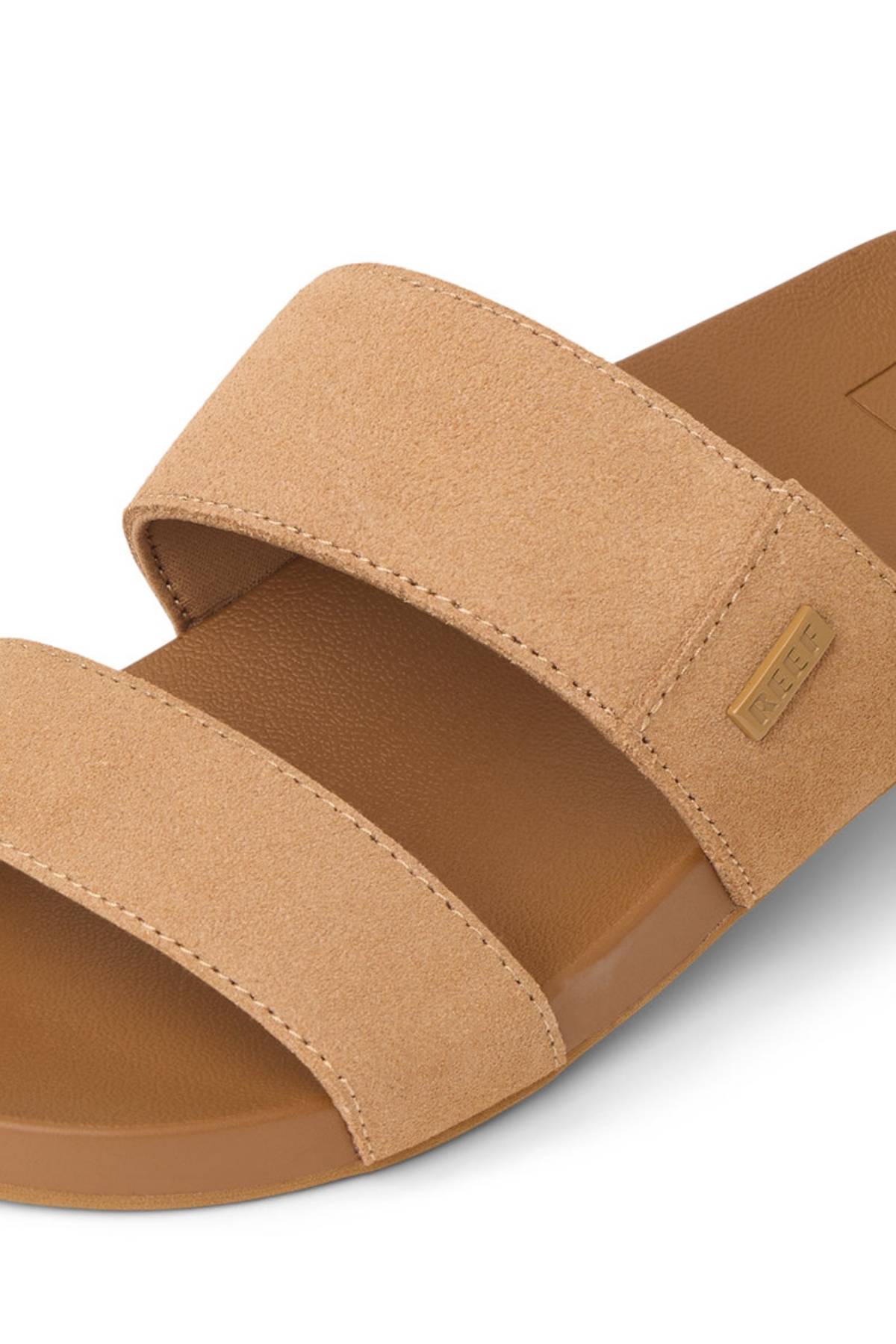 Close-up of the REEF Cushion Vista Stevie sandal in tan, featuring two wide suede straps, a brown sole, a small stitched label on the upper strap, and subtle arch support for added comfort.